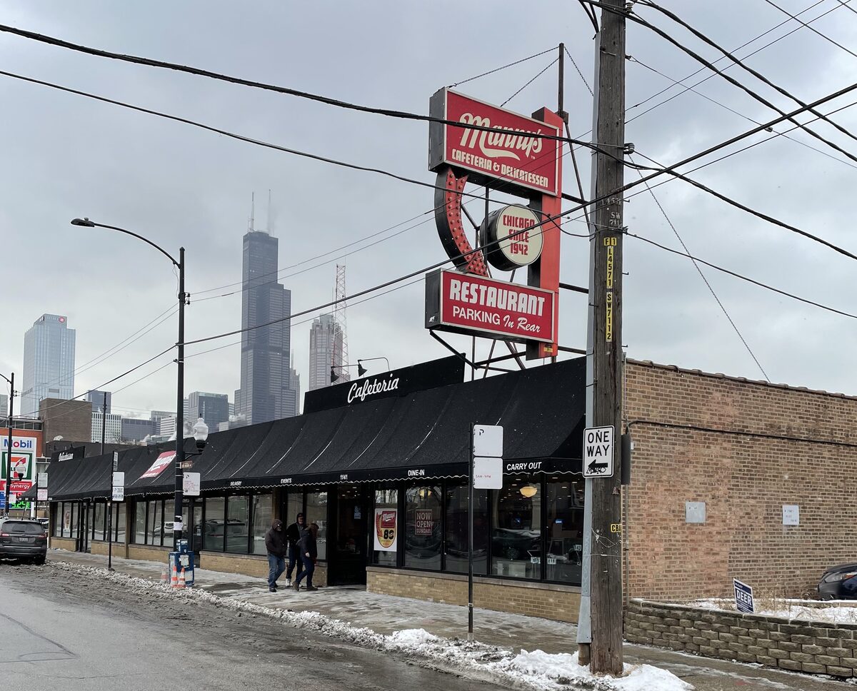 The red Manny's Deli sign above the low brick building, with downtown towers behind