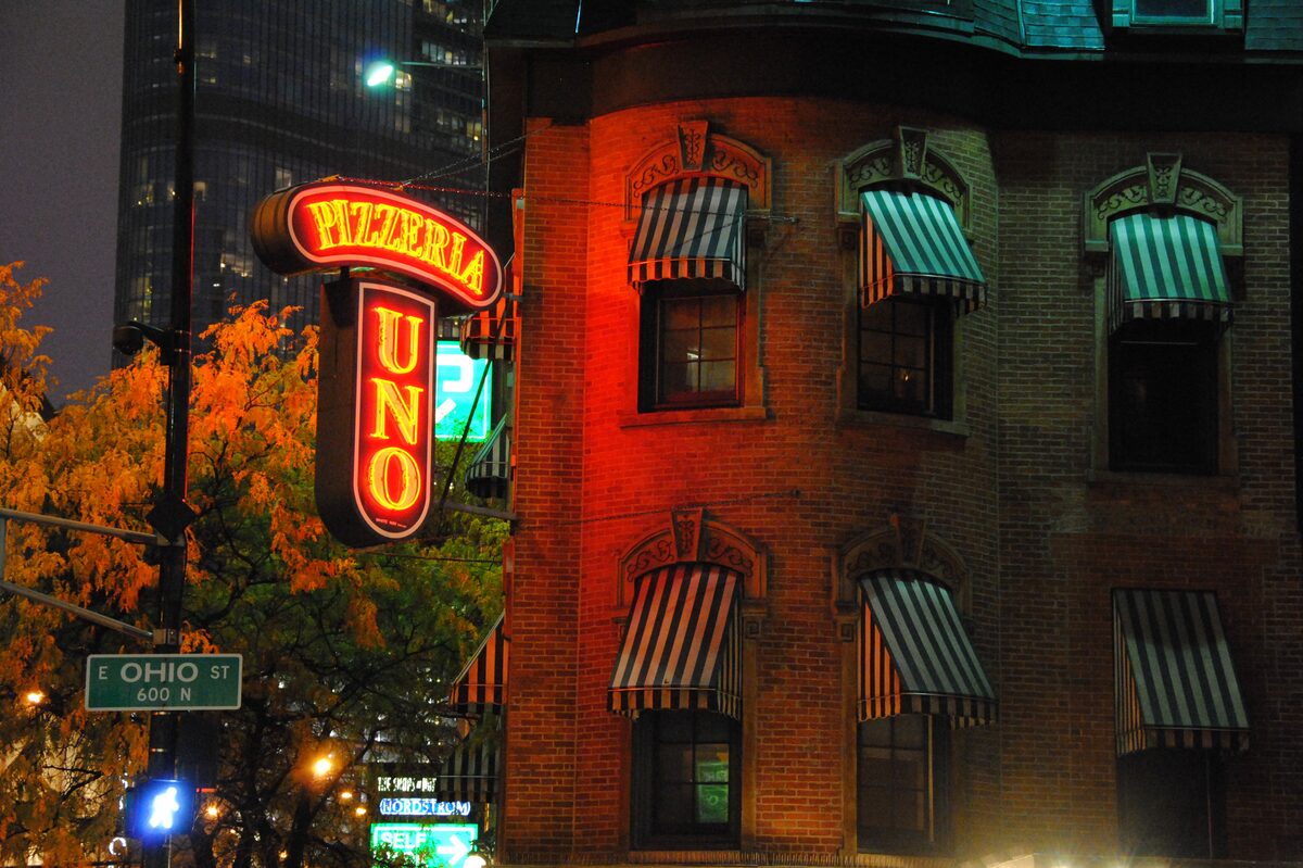 The red neon Pizzeria Uno sign on the brick corner building at dusk