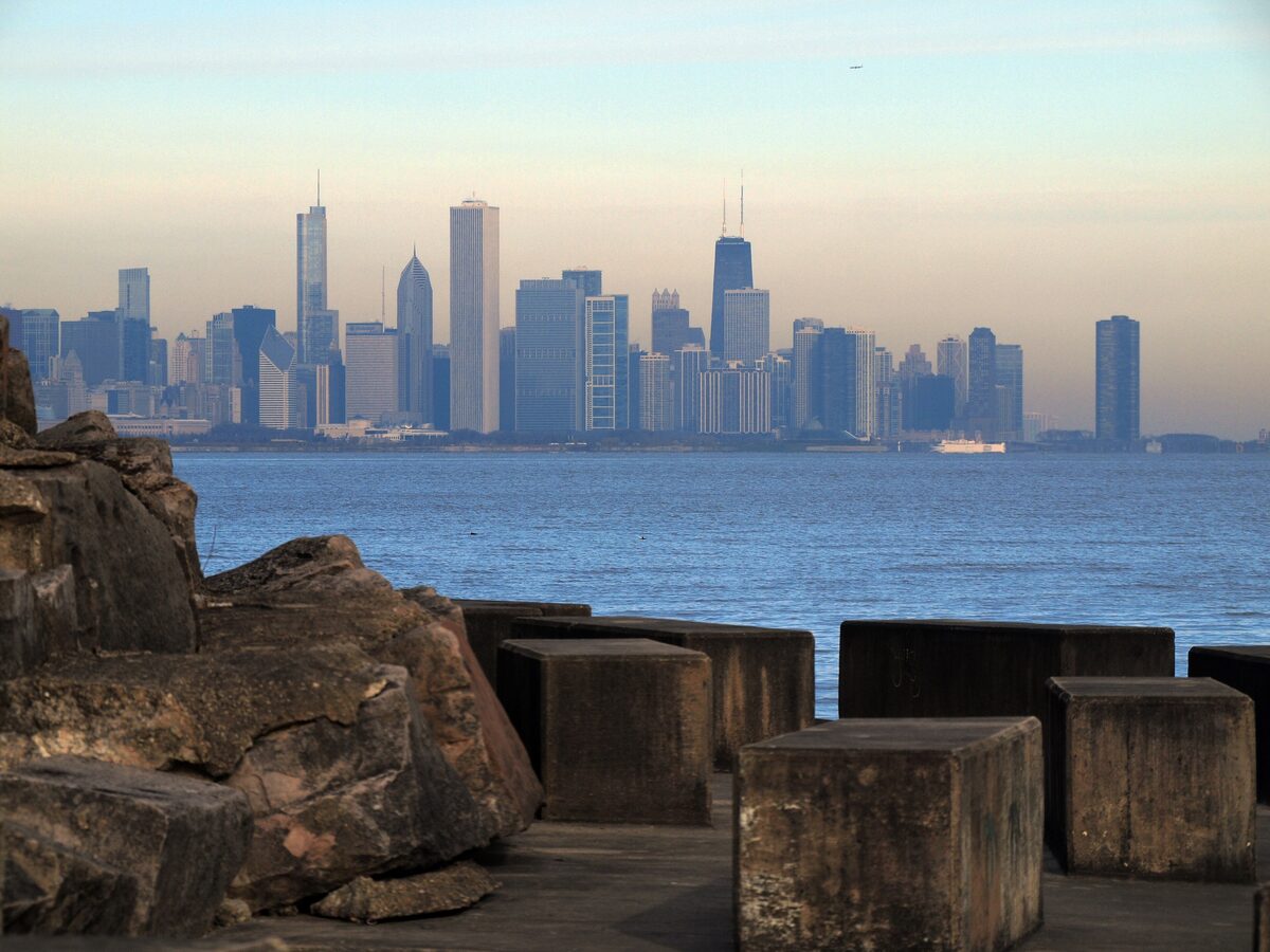 The Chicago skyline across the lake at dusk, seen over limestone blocks at Promontory Point