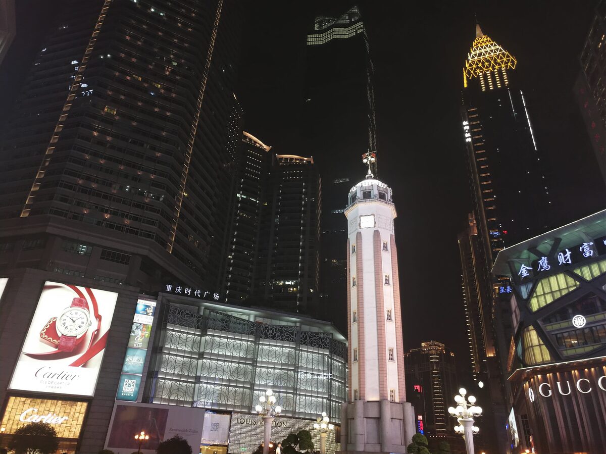 The white Jiefangbei monument tower lit at night among glass skyscrapers and shop signs