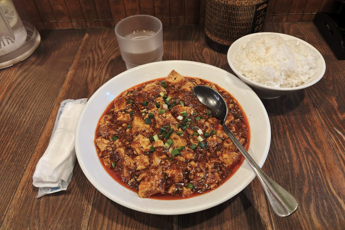 A plate of mapo tofu in red chili sauce with scallions, served with a bowl of white rice