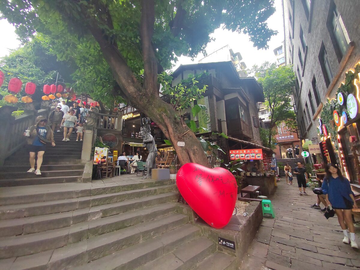 Stone steps on Shancheng Alley lined with shops and red lanterns, with a big tree and a red heart sculpture