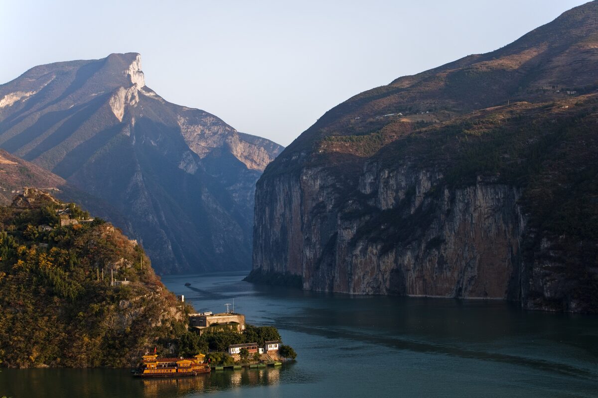 Qutang Gorge on the Yangtze, with steep cliffs closing in over the river and a golden tourist boat moored at a small riverside settlement