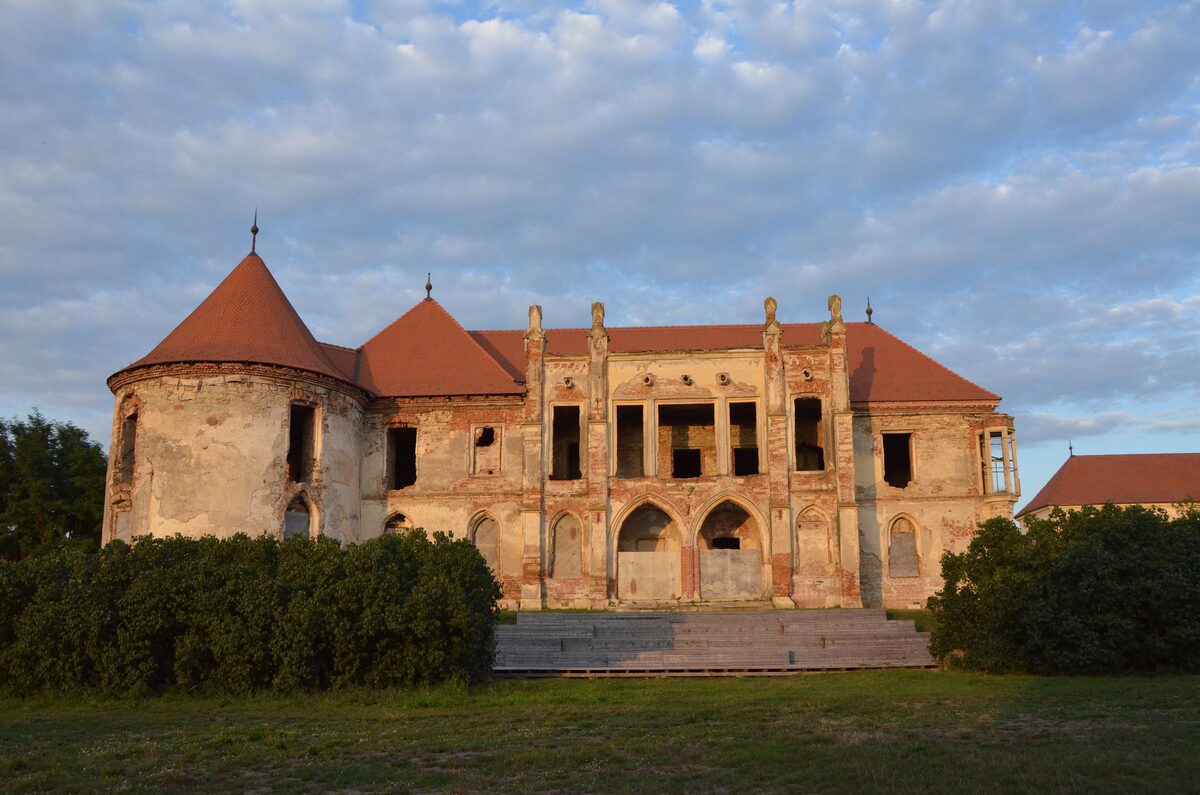 The roofless baroque main front of Bánffy Castle in Bonțida, with its round corner tower and red roofs, in evening light