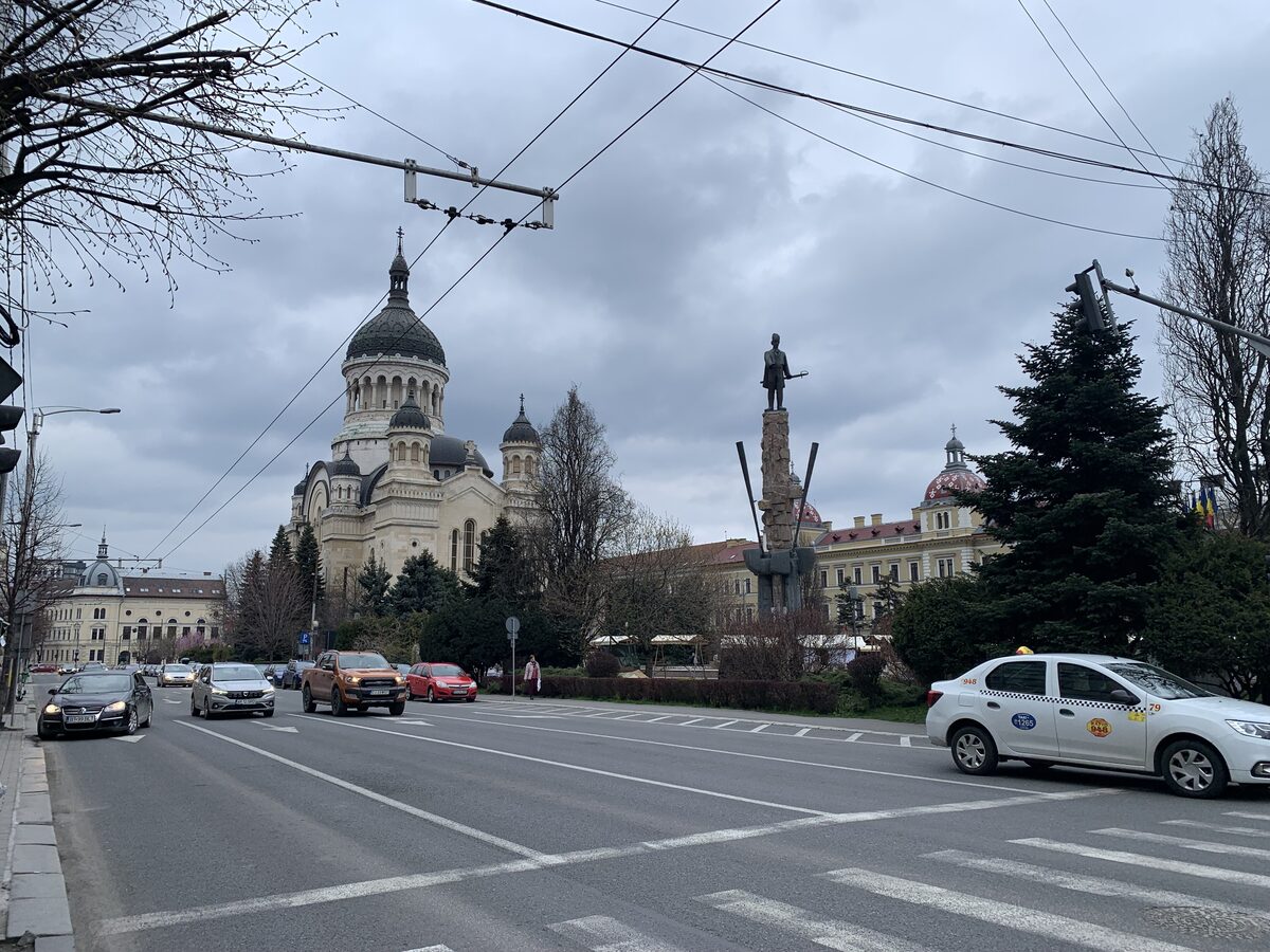 The domed Orthodox Metropolitan Cathedral and the Avram Iancu statue on Avram Iancu Square, seen down a wide street under a cloudy sky