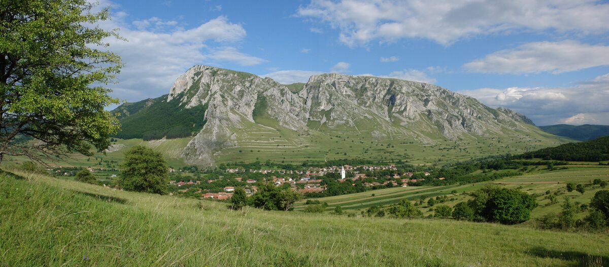 The village of Rimetea with its white church tower, in green meadows below the jagged limestone ridge of Piatra Secuiului