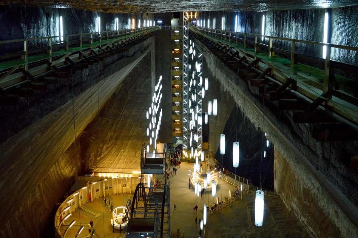 Looking down into the vast Rudolf chamber of the Turda Salt Mine, with salt walls, hanging lights, the lift tower and the attractions on the floor far below