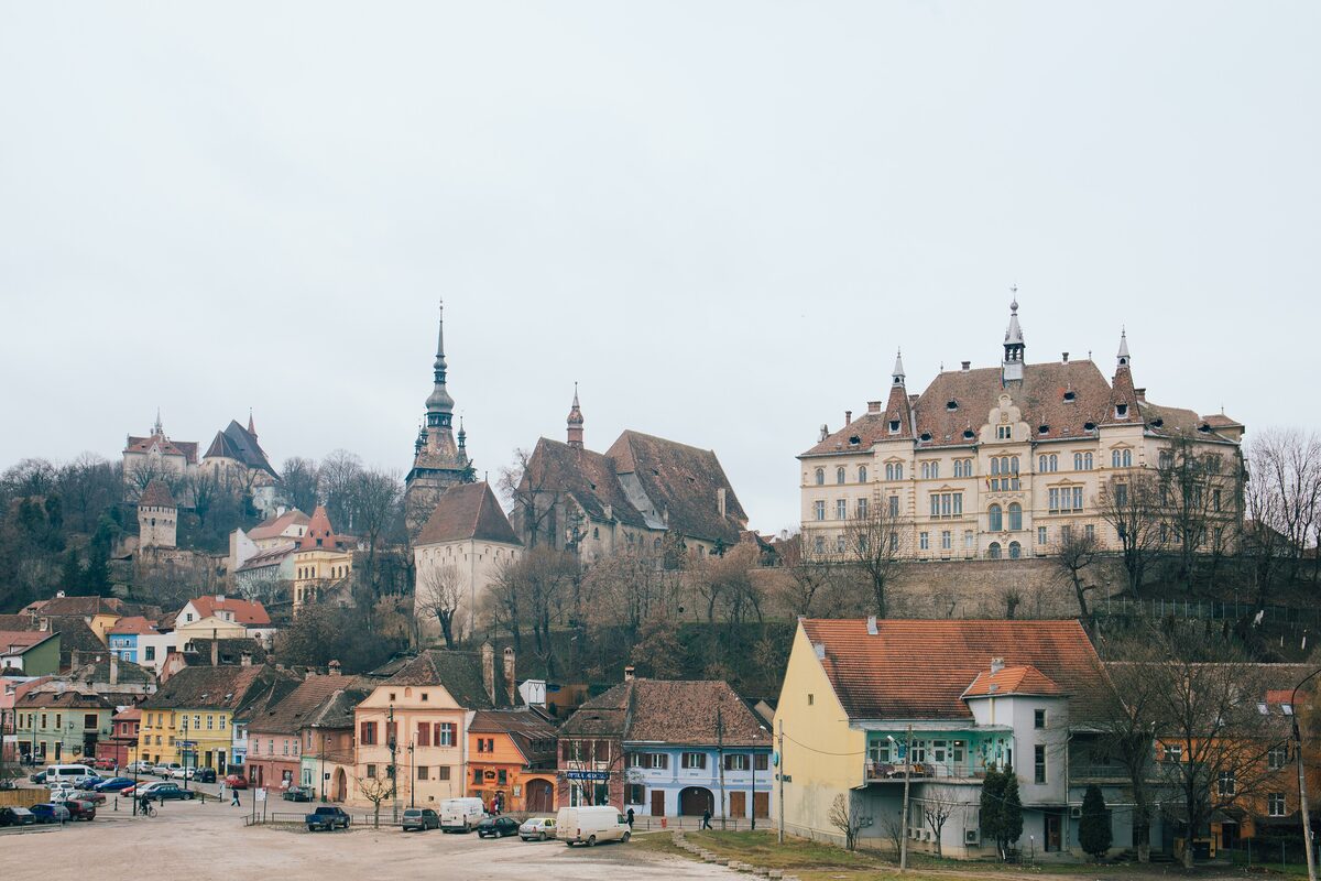 The hilltop citadel of Sighișoara with its clock tower, church spires and a large yellow building above colorful houses
