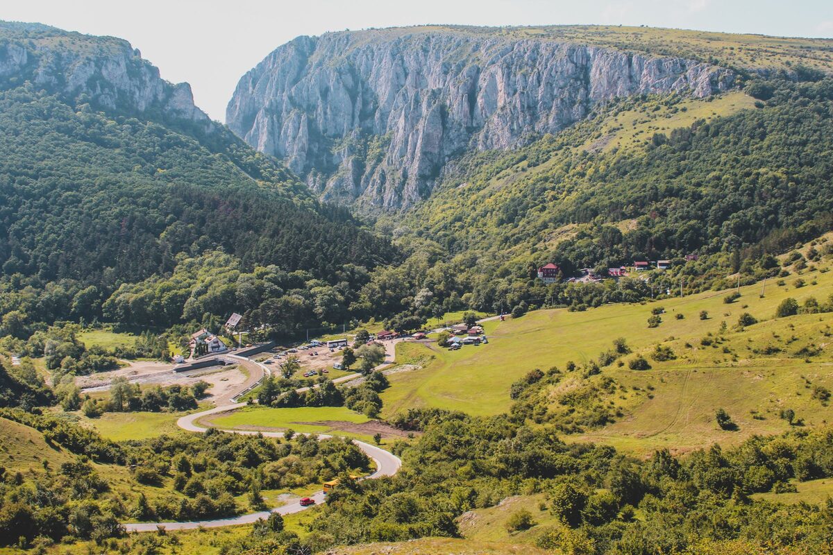 The limestone cliffs of Turda Gorge rising above green wooded slopes, with meadows in the valley below