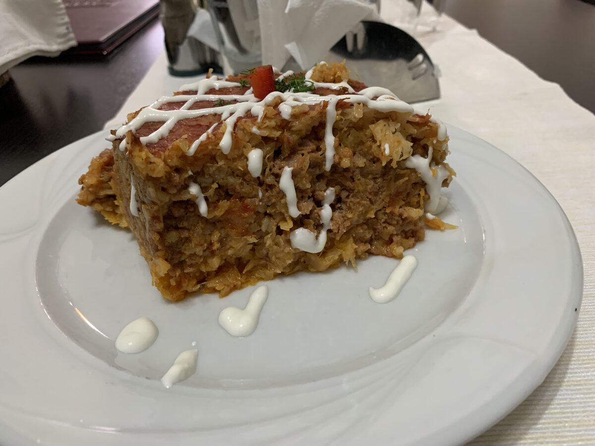 A thick slice of layered varză à la Cluj on a white plate, drizzled with sour cream
