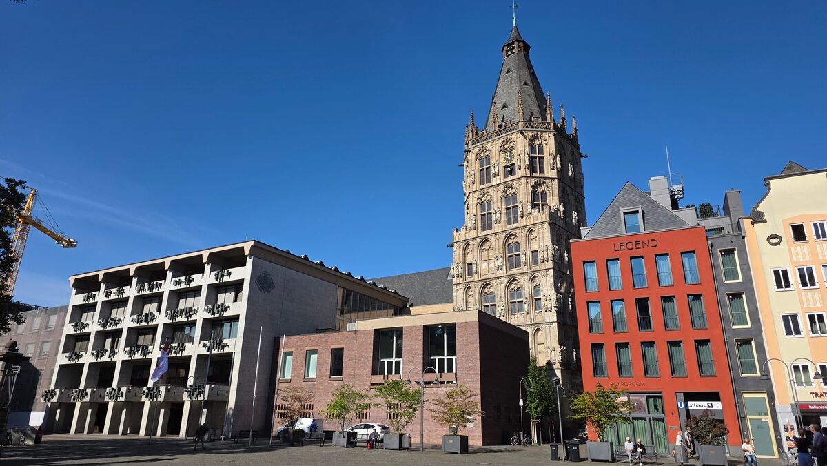 The Gothic tower of Cologne's town hall above modern buildings on Alter Markt under a blue sky