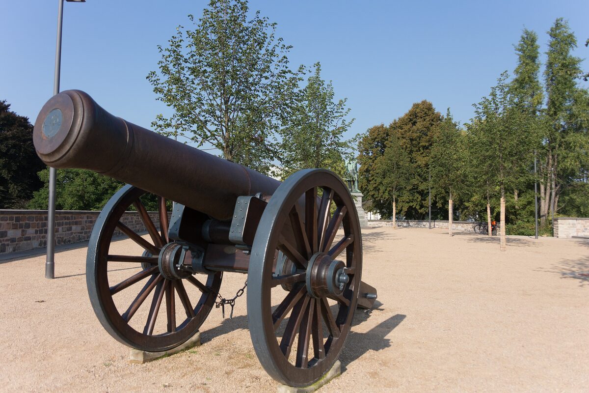 An old iron cannon on the sandy terrace of the Alter Zoll bastion in Bonn, with trees behind