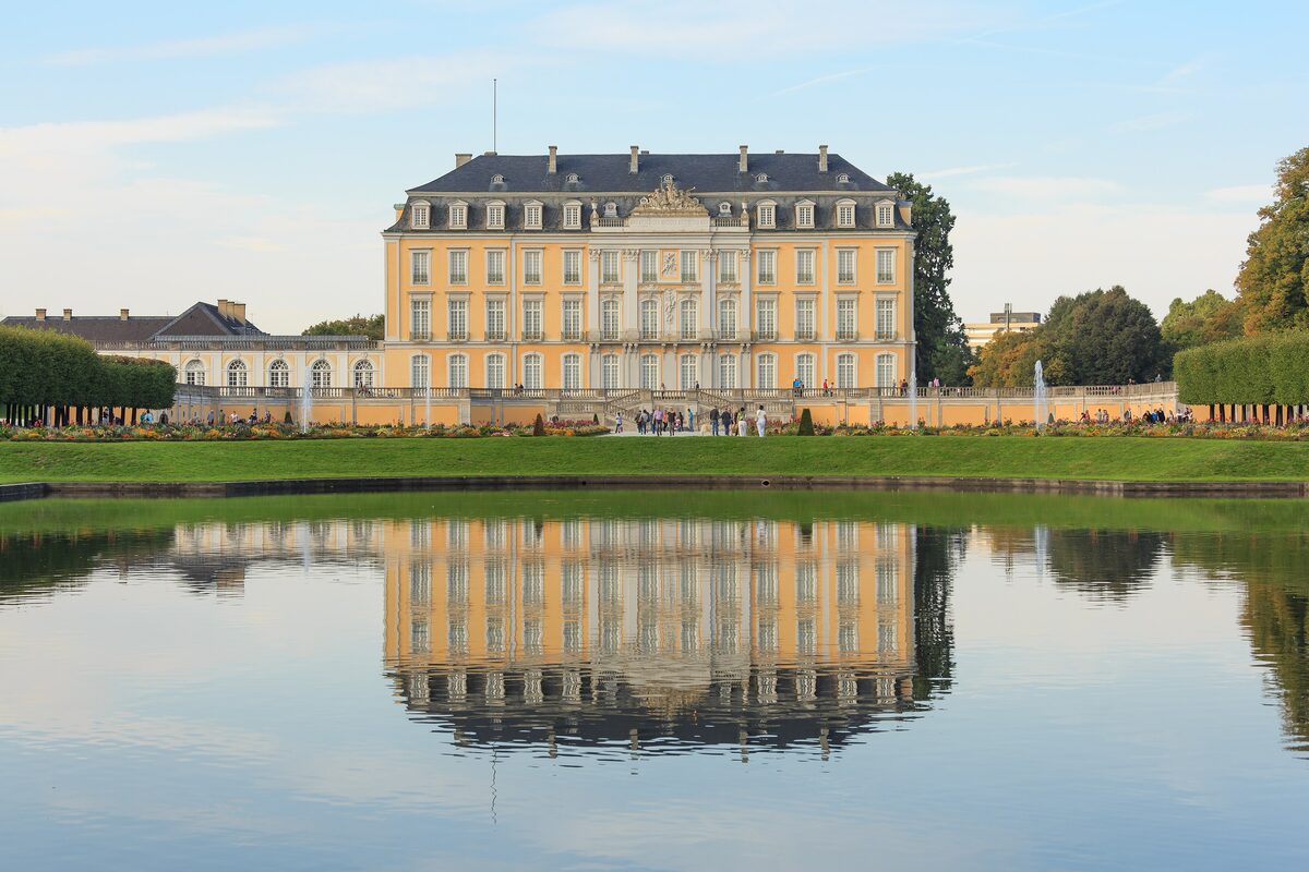 The yellow facade of Augustusburg Palace mirrored in a pond in the park