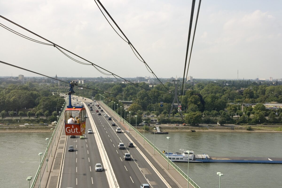 A red cable car gondola above the Zoo Bridge and the Rhine, seen from another cabin