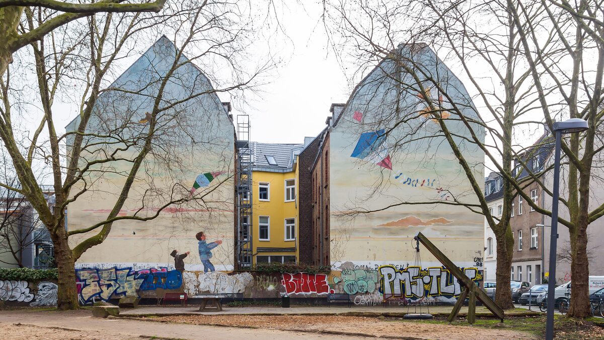 A large mural across two facing gable walls in Ehrenfeld, painted with sky and a child