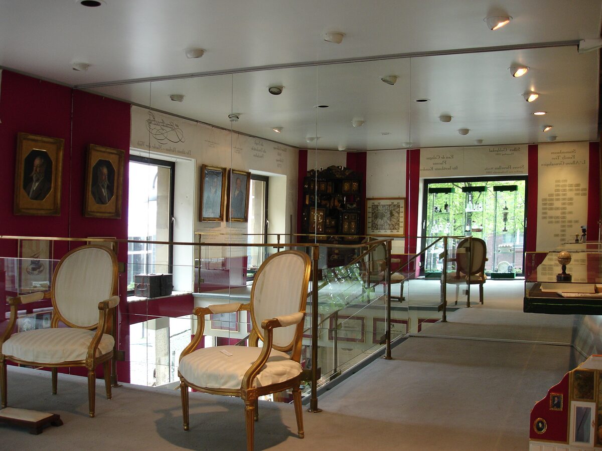 A first-floor room of the Farina fragrance museum with two upholstered armchairs, framed portraits and glass display cases