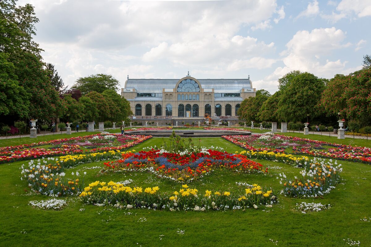 The glass-and-iron Flora hall behind round flower beds in full bloom