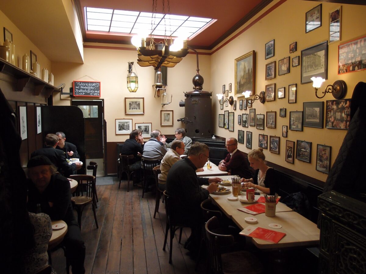 Guests at long tables in the wood-paneled dining room of Früh em Veedel, with framed pictures on the walls