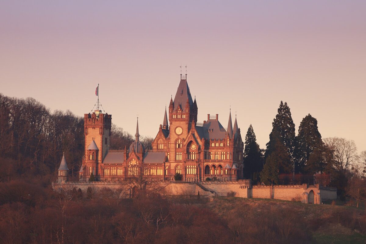Drachenburg Castle with its towers and gables on a wooded hillside at sunset