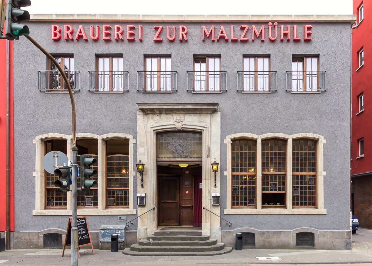 The gray corner house of the Brauerei zur Malzmühle with its red sign and entrance steps