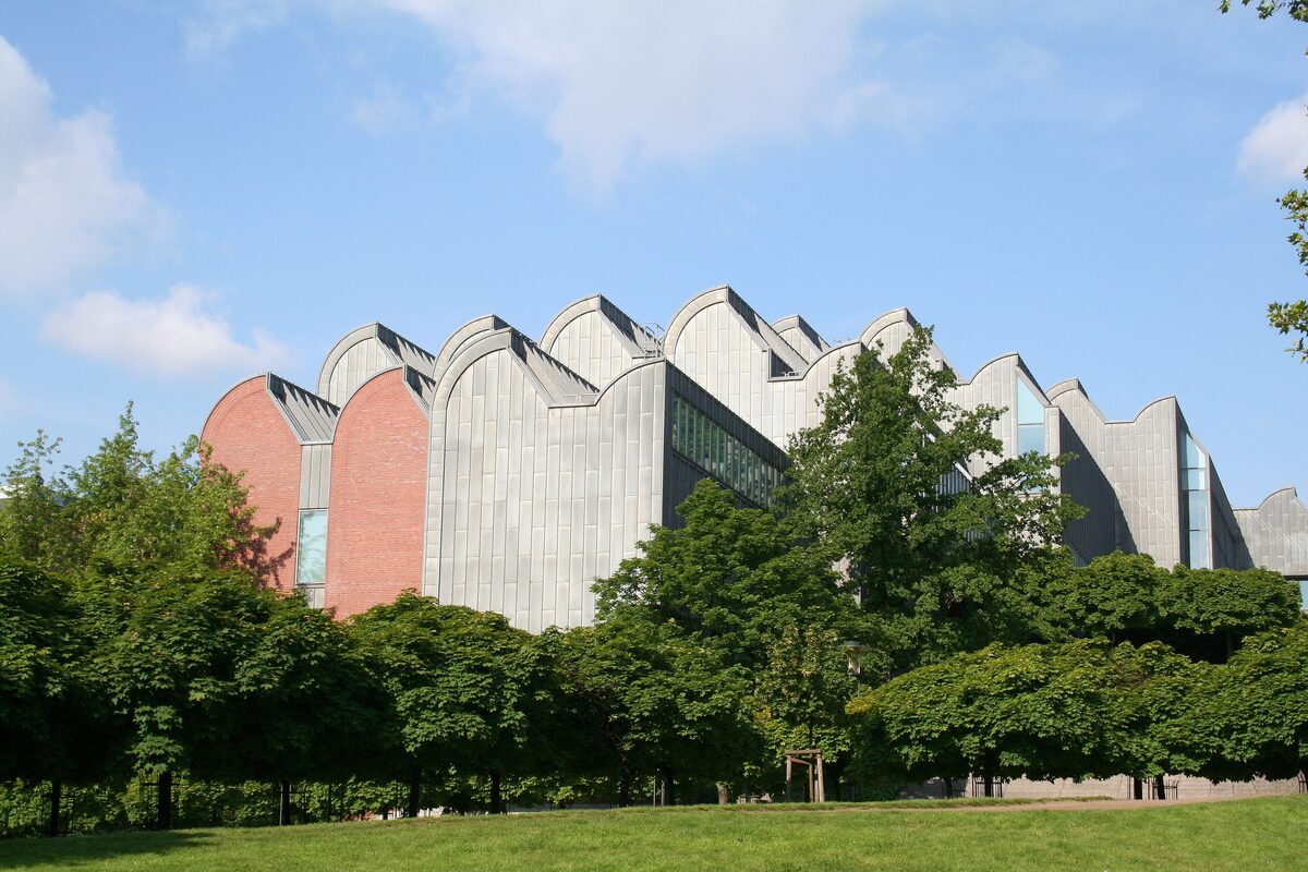 The sawtooth roofs of Museum Ludwig seen across a lawn and trees