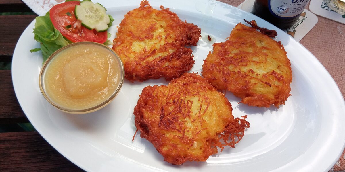 Three golden potato pancakes with a bowl of apple sauce and a small salad
