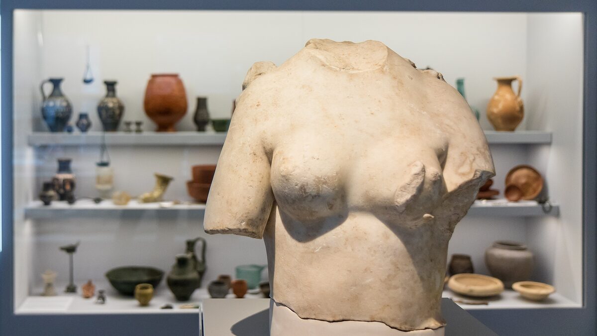 A Roman marble torso and small pottery vessels in a display case at the Roman-Germanic Museum