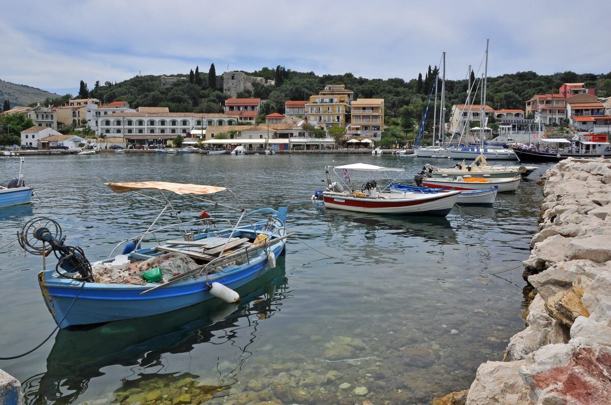 Colorful fishing boats in the little harbor of Kassiopi, with waterfront buildings and green hills behind