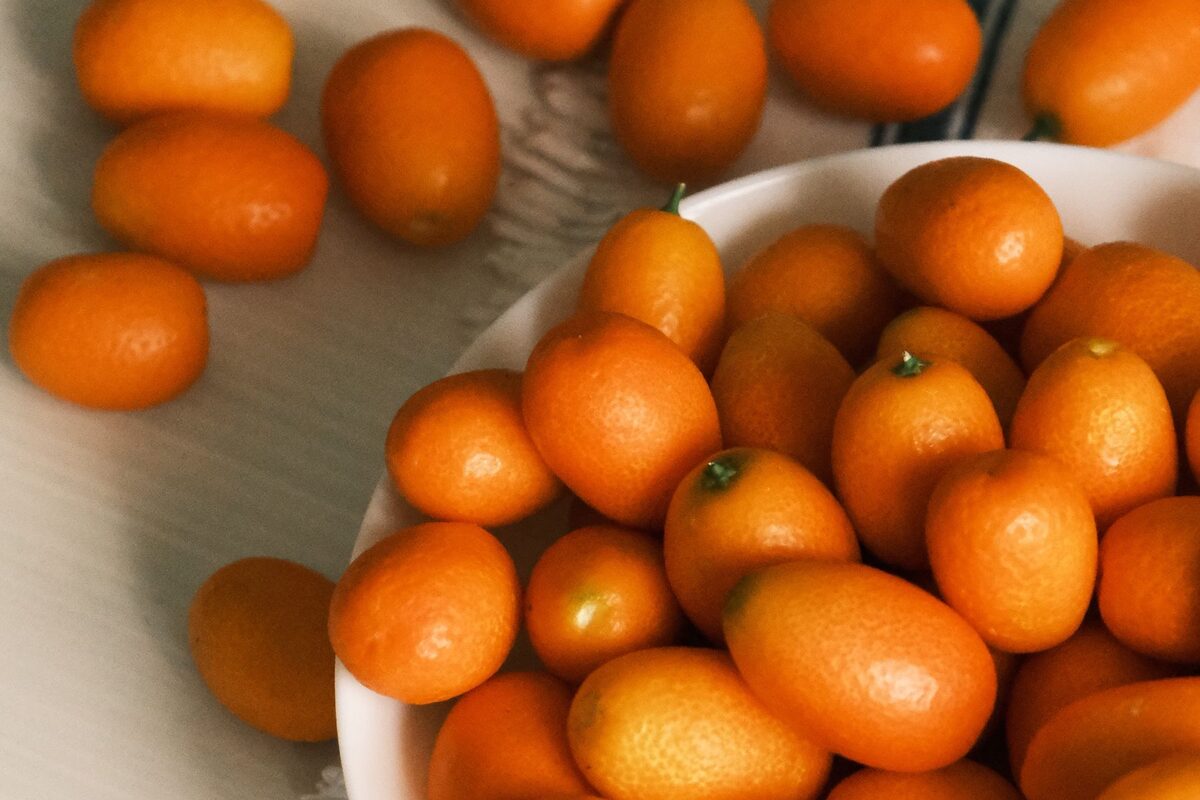 A white bowl of small, bright orange kumquats on a striped cloth