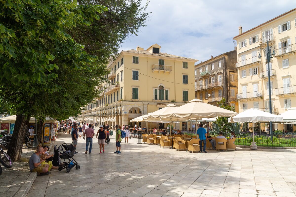 The Liston arcades and café terraces under trees at the edge of the Spianada, with tall Venetian-style buildings behind