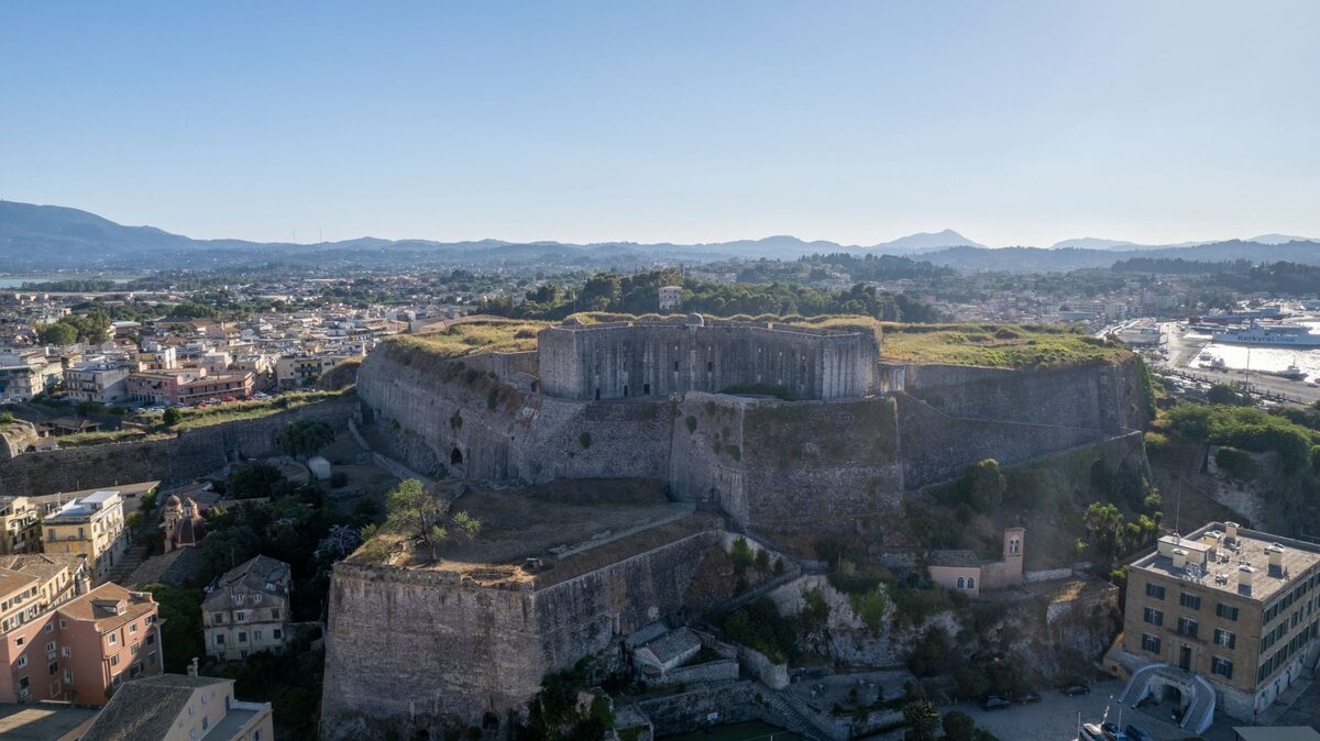 Aerial view of the massive stone bastions of the New Fortress of Corfu rising above the old town, with the island and mountains behind