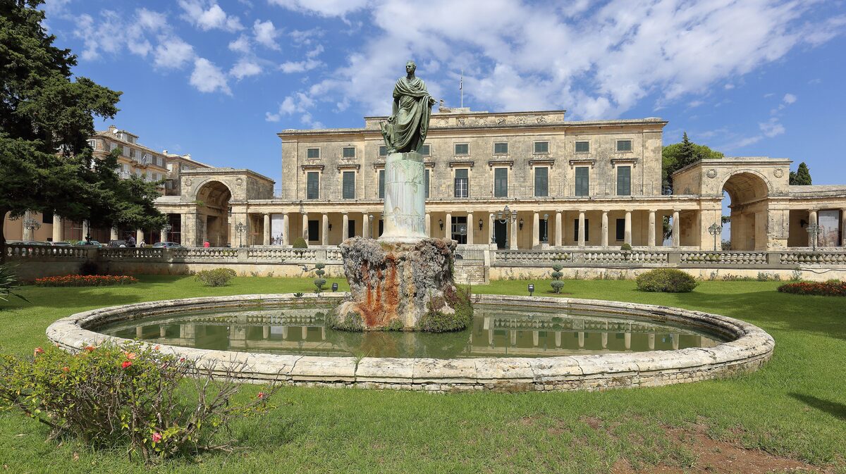 The colonnaded Palace of St. Michael and St. George in Corfu, with a statue and round fountain on the lawn in front