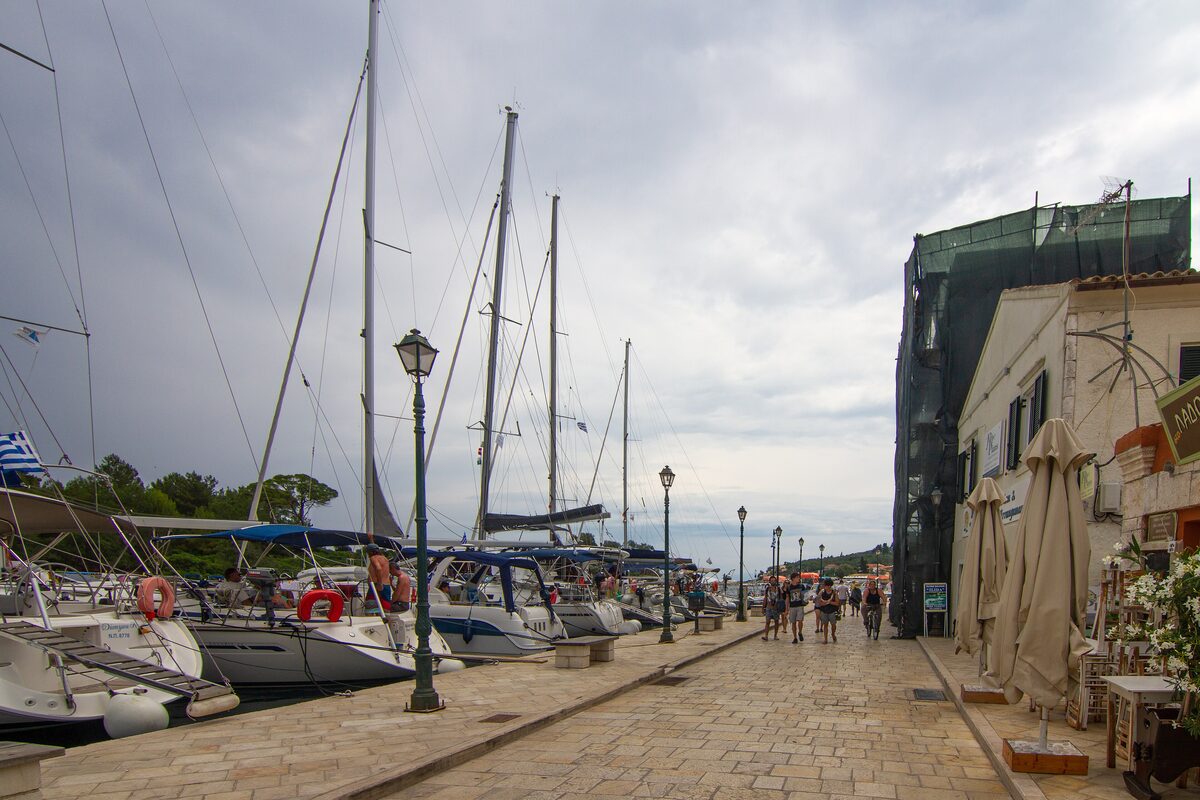The harbor promenade of Gaios on Paxos, with sailing boats moored along the quay and old houses behind