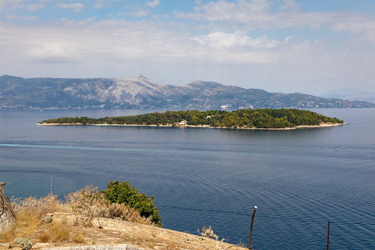 The small green island of Vido in the blue sea off Corfu Town, with the mountains of the mainland behind