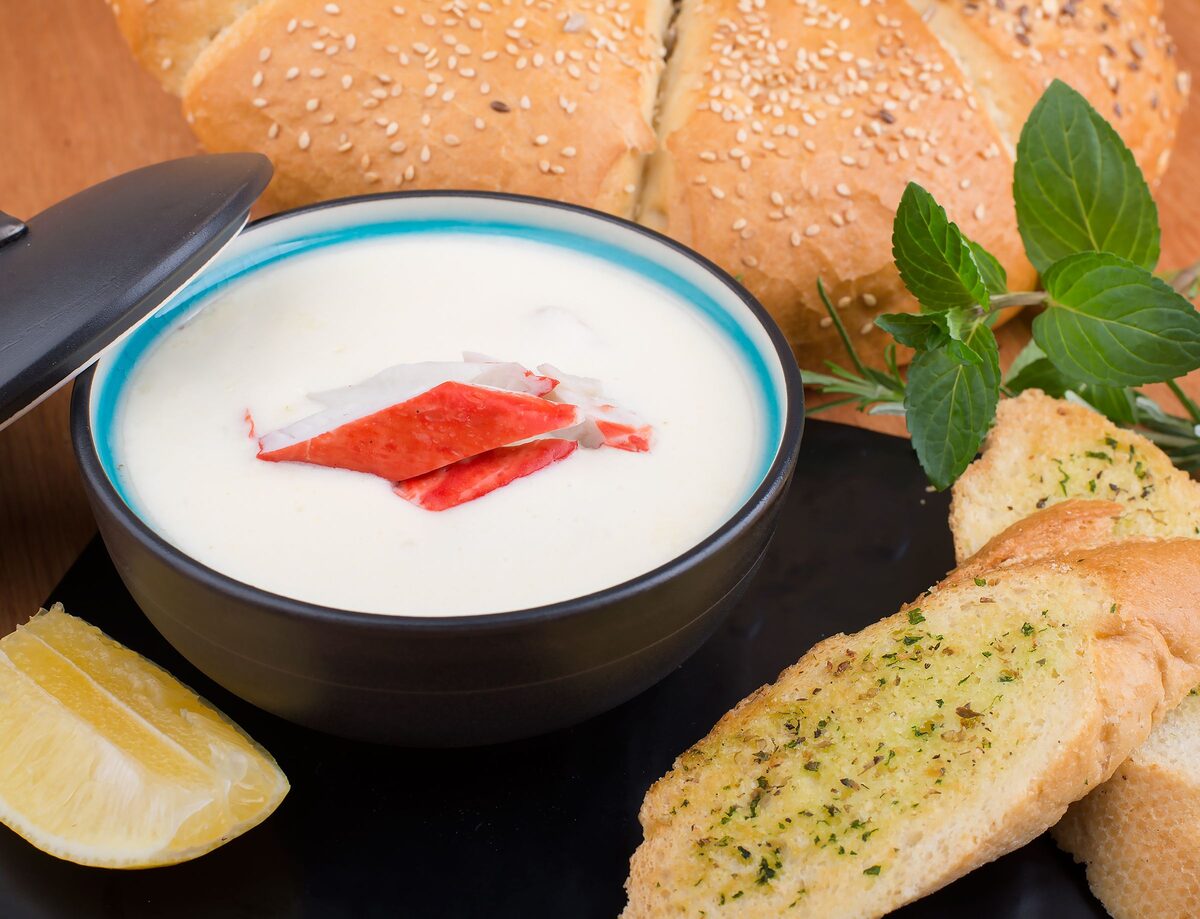 A bowl of creamy seafood chowder with garlic bread and a lemon wedge