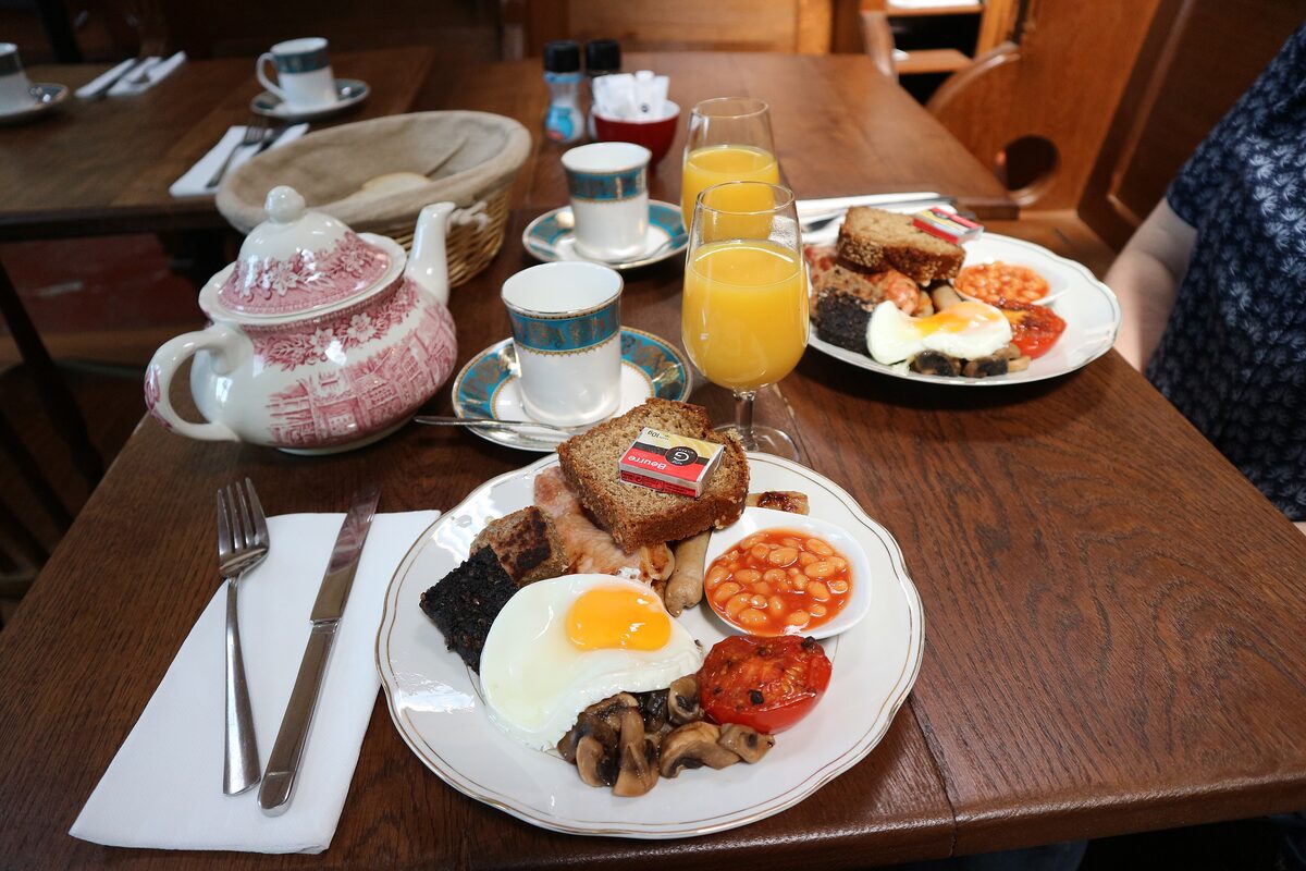 A full Irish breakfast with fried egg, black pudding, sausage, bacon, beans, mushrooms and tomato, with tea and orange juice on a wooden table