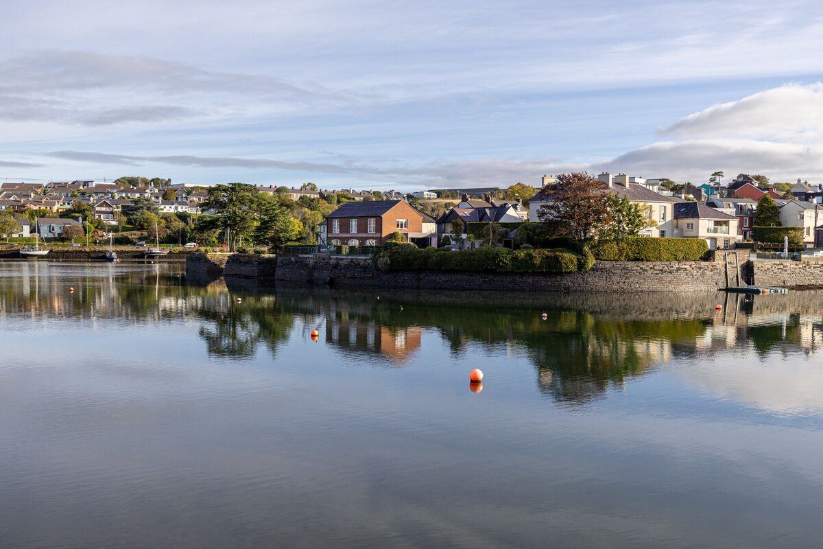 Colorful houses along the water in Kinsale reflected in the calm harbor, under a cloudy sky
