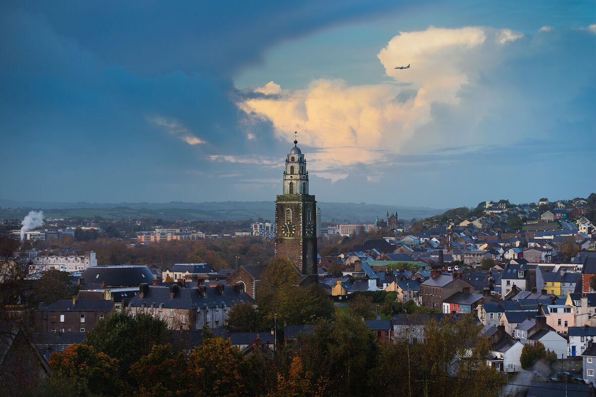 The tower of St Anne's Shandon with its golden weathervane rising above the houses of Cork's north side, under an evening sky