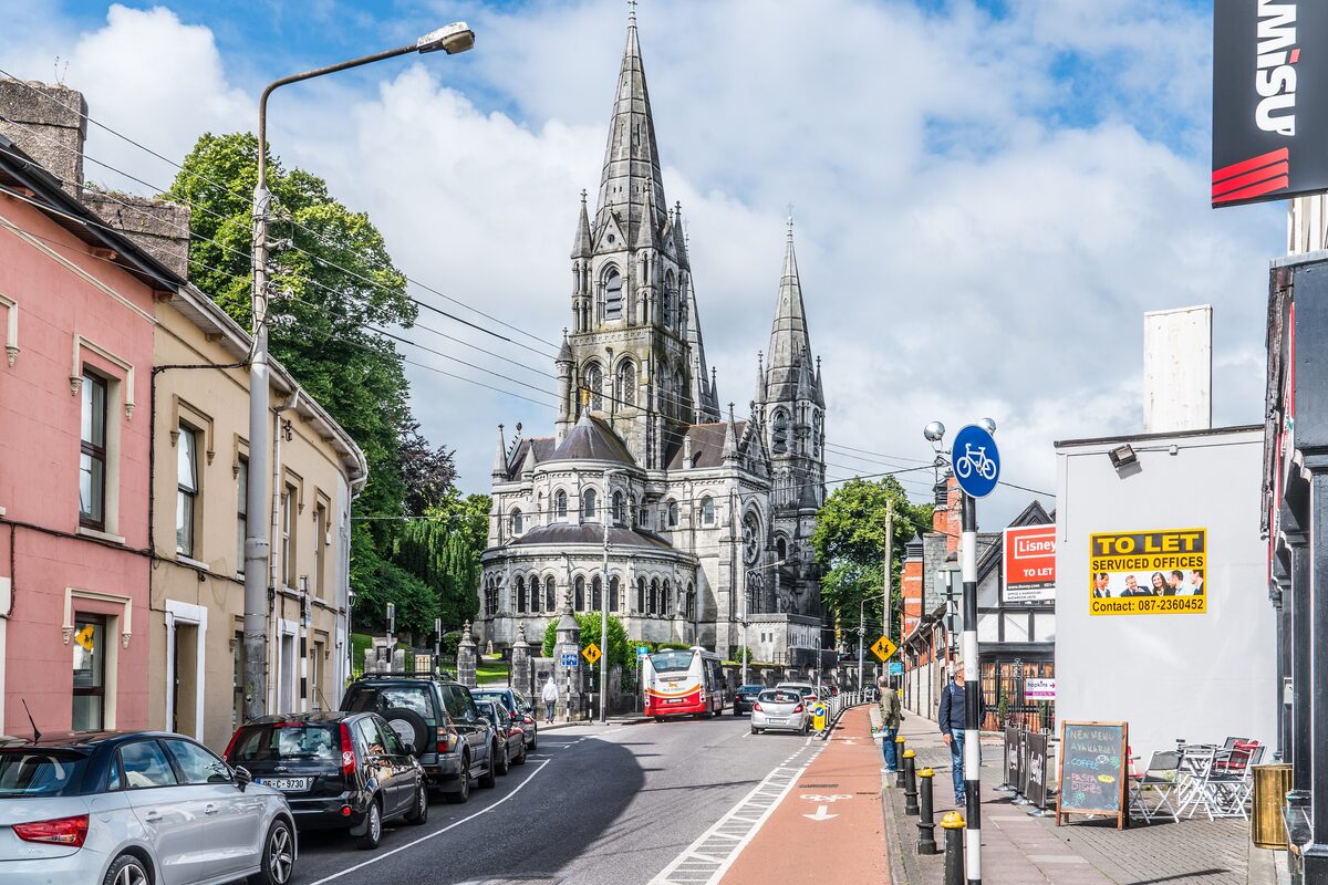 The three Gothic spires of St Fin Barre's Cathedral rising at the end of a Cork street lined with colorful houses