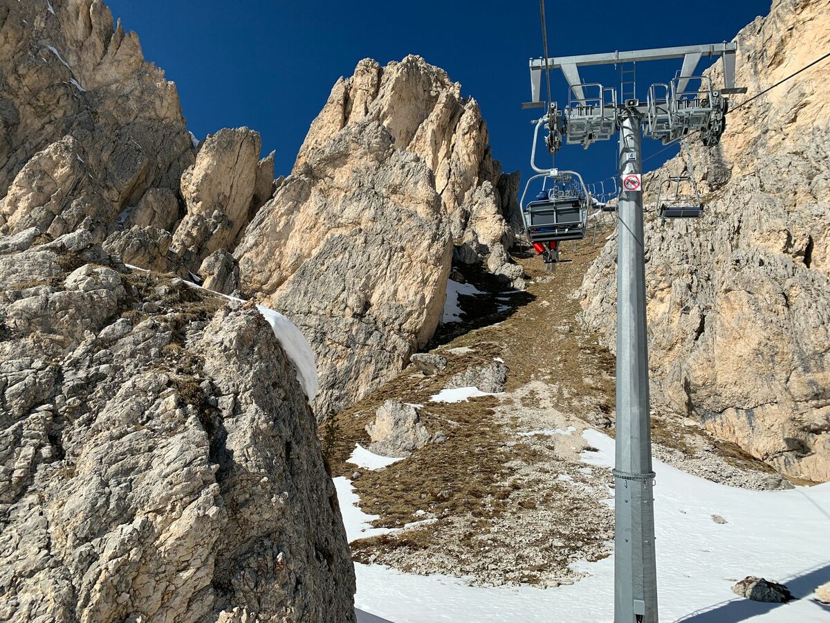 A chairlift passing between pale rock spires in the Dolomites, with patches of snow on the ground below