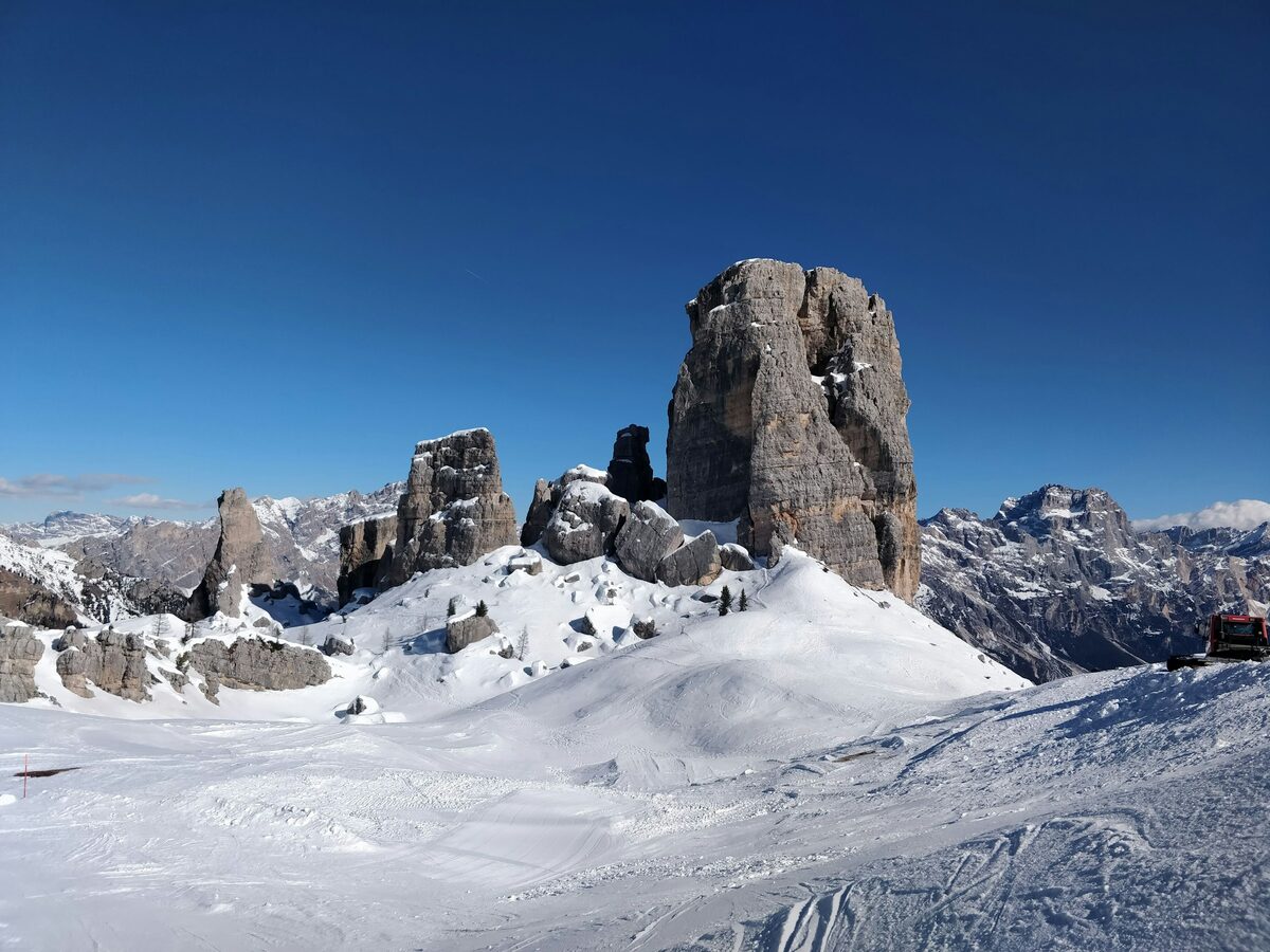 The rock towers of the Cinque Torri rising above a snowy ridge under a deep blue sky