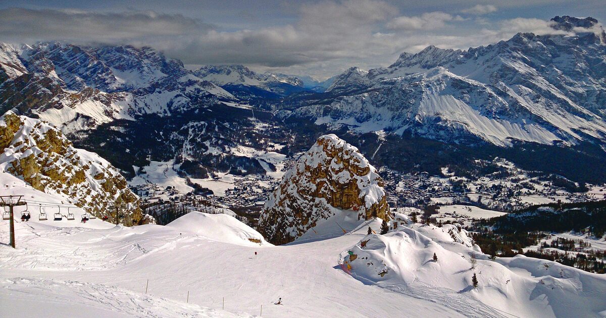 Snowy ski slopes and a chairlift in the foreground, the town of Cortina in the valley and the Dolomite peaks beyond