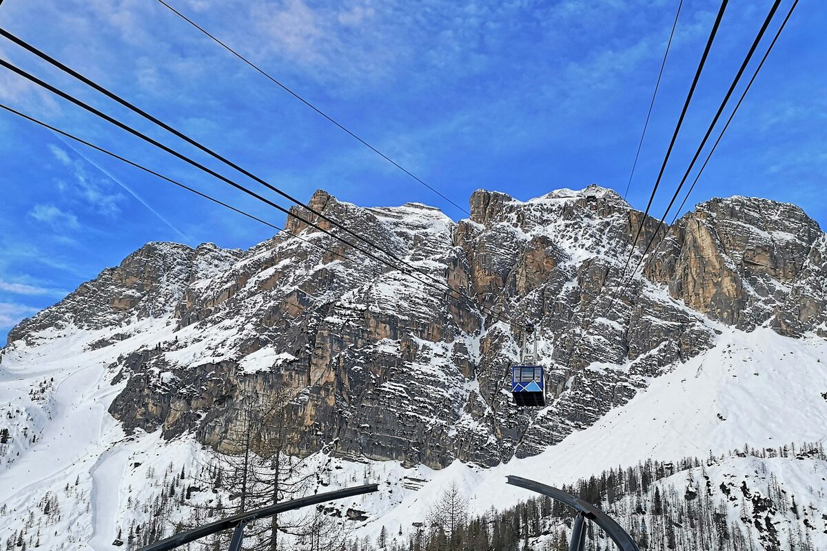 A cable car cabin on its cables above a snowy rock face under a blue sky