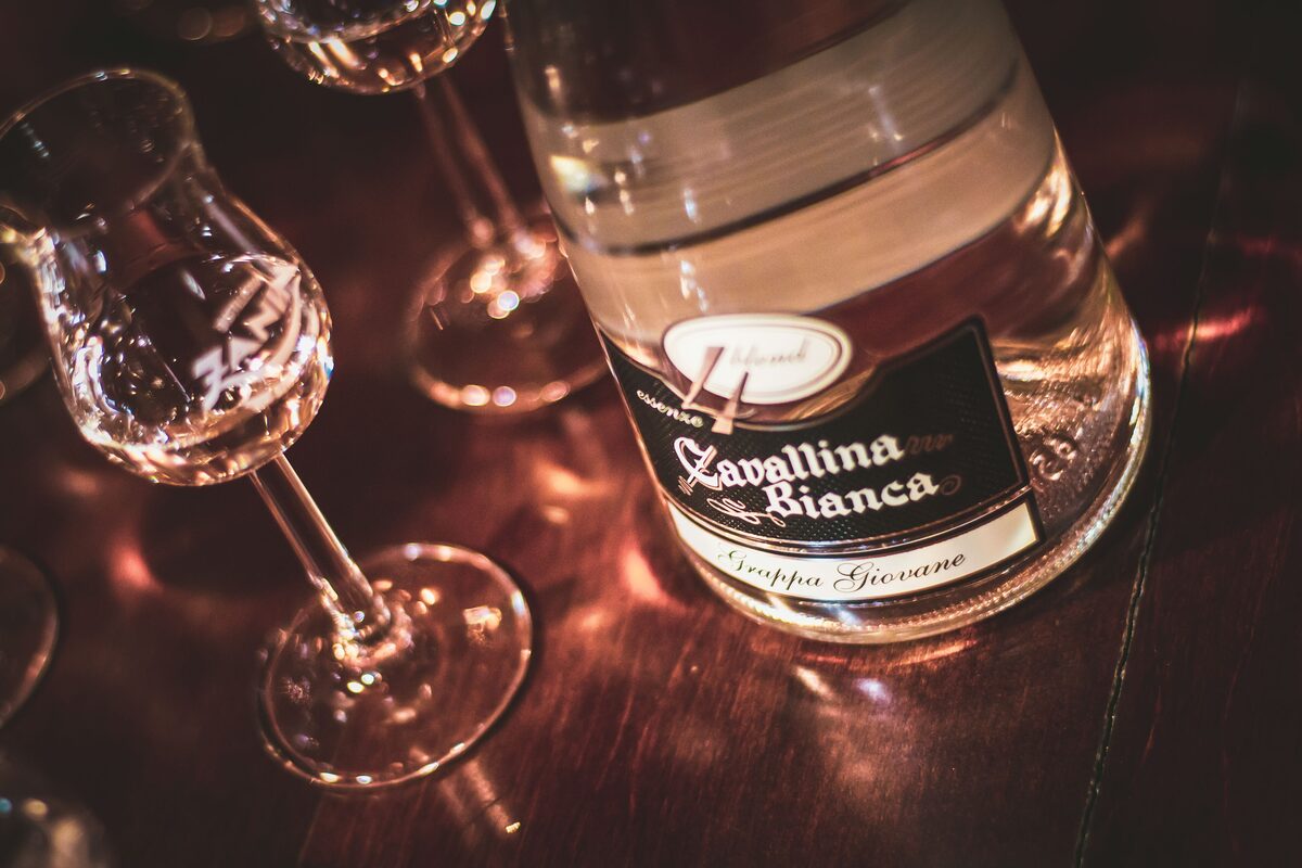 A bottle of grappa and tasting glasses on a dark wooden table