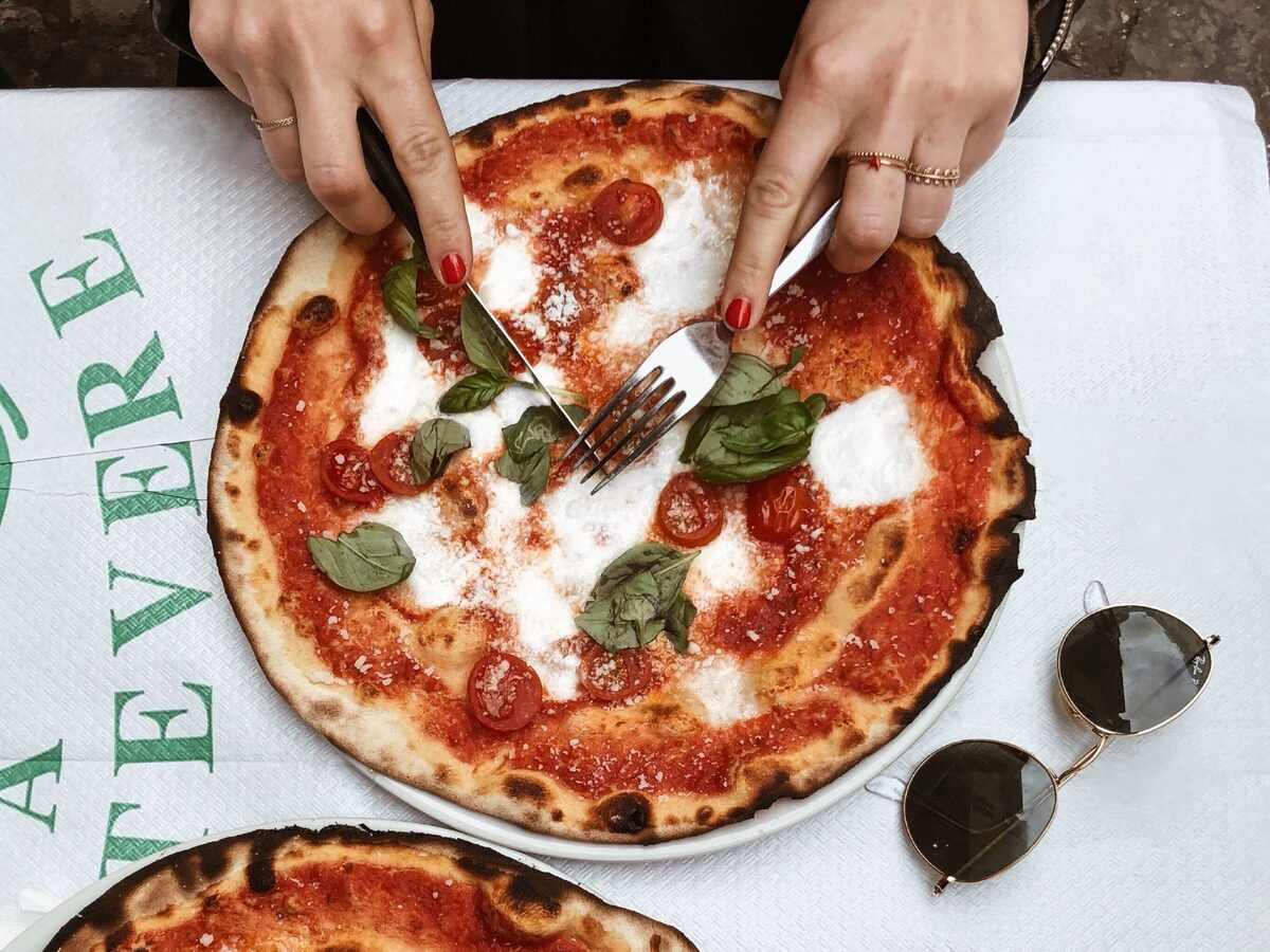 A Margherita pizza with charred crust, mozzarella and basil on a paper tablecloth, seen from above and eaten with knife and fork