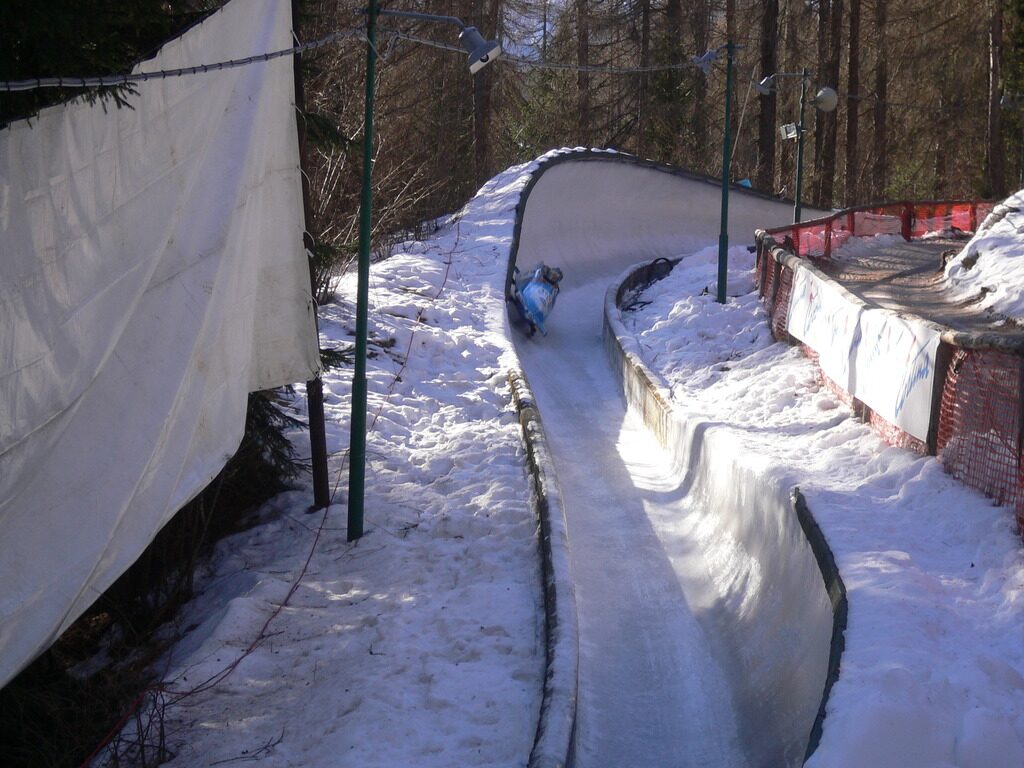 The snow-lined bobsleigh run of the Eugenio Monti track in Cortina, with a sled in the distance