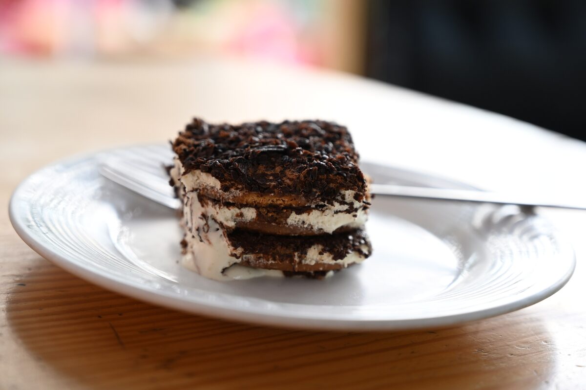 A square slice of layered tiramisu with a dark grated topping, on a white plate