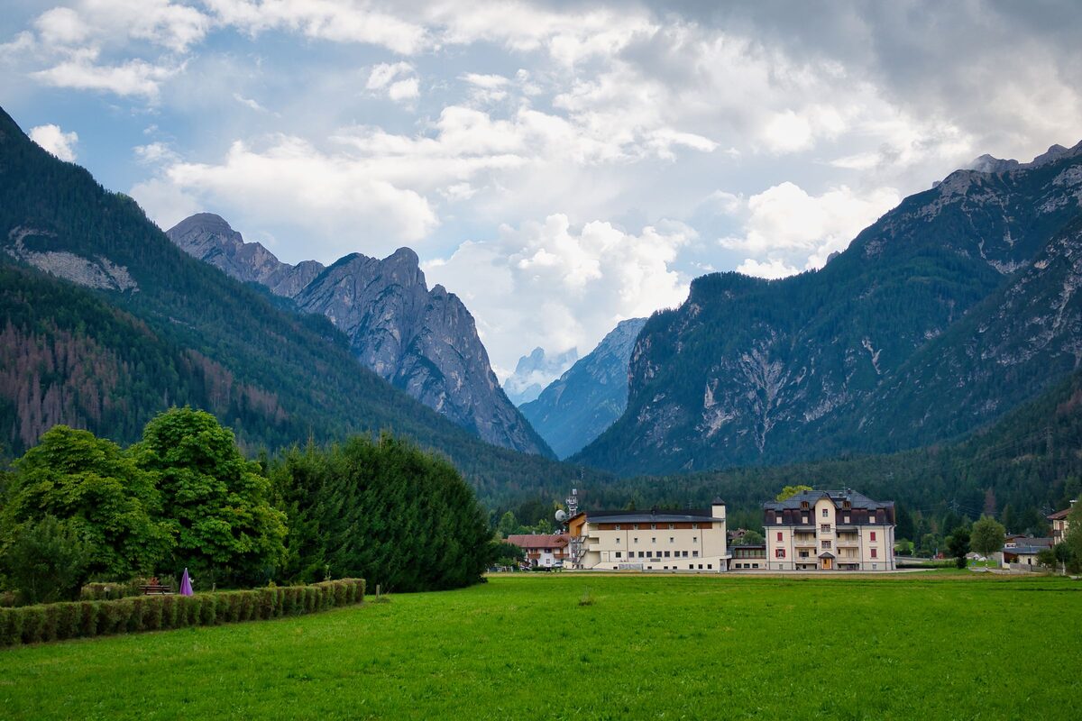 Green meadow in the Toblach valley with a large hotel building at the foot of forested Dolomite mountains