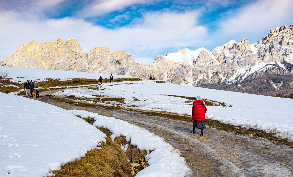 Walkers on a snowy valley track on a sunny day, with sunlit Dolomite ridges behind