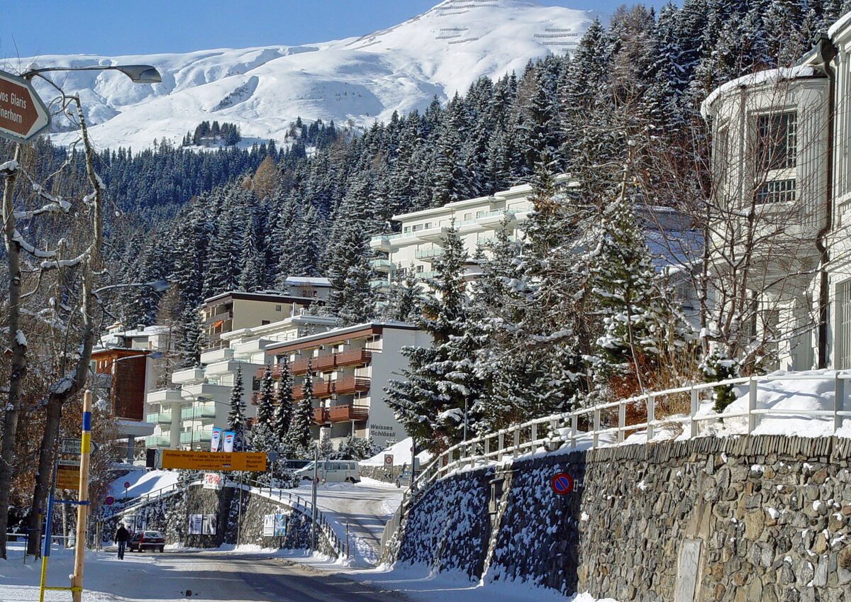 Hotels on a snowy hillside in Davos, with pine forest and snow-covered mountains behind